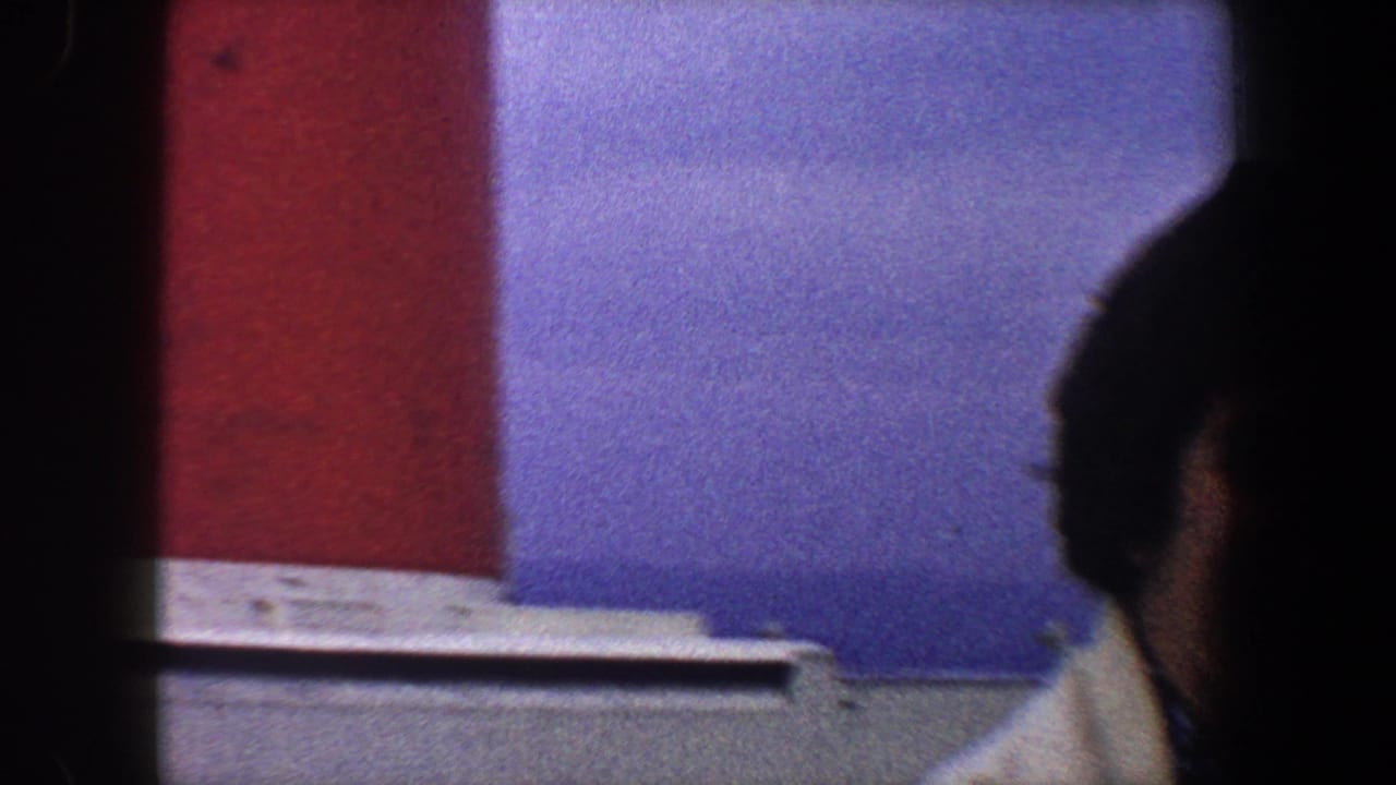 Partial view of a person at frame edge with a red smokestack and blue sky behind.