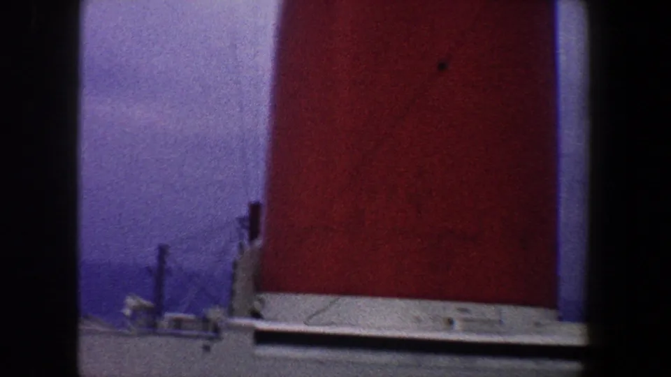 The red smokestack remains in view with a pale ledge and blue sky, framed by the handheld 8mm camera.