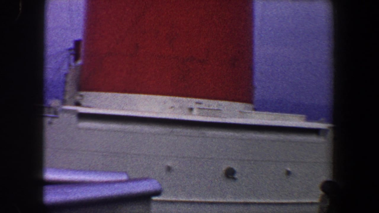 1960 New York City home-movie frame showing a red ship funnel, white superstructure, railing, and dark vertical foreground bars.