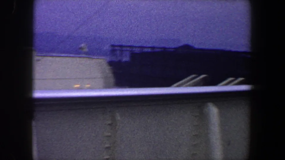 White vessel structure and railing appear against a dark distant shoreline in this 1960 New York City ship-deck view.