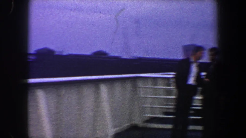 Two blurred adults appear near railings and white deck panels during the 1960 New York City ship pan.