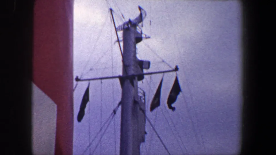 A ship mast with rigging and hanging flags appears beside the red and white vessel structure in the 1960 New York City footage.