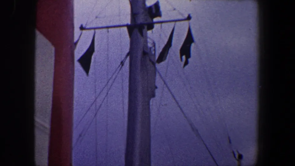 1960 New York City home-movie frame showing a passenger ship mast with flags, red funnel, vents, and upper deck details.