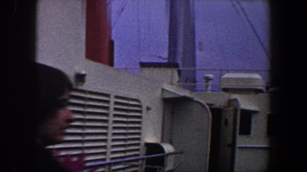 A woman passes along a ship deck near vents and a doorway.