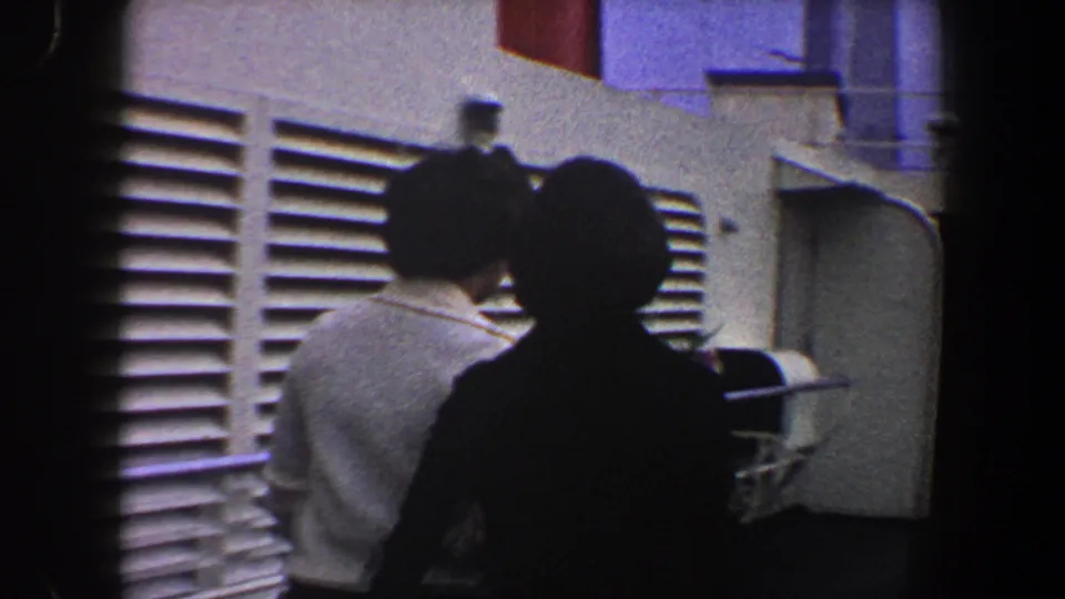 Two women are seen from behind on a passenger ship deck in 1960 New York City, near white ventilation grilles and deck hardware.