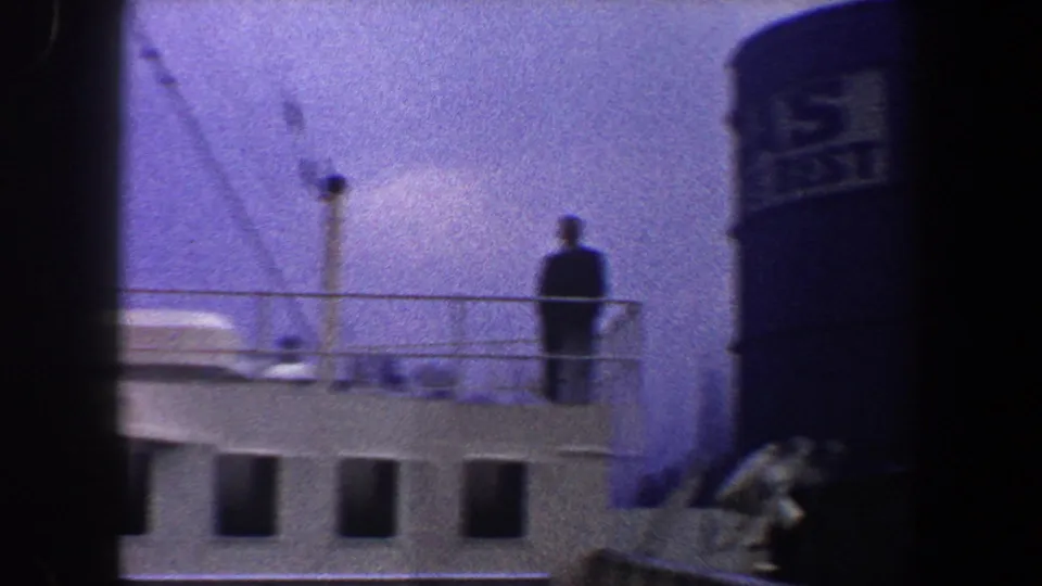 A man stands on an upper deck of a large passenger ship in 1960 New York City, with railings, mast lines, and a funnel nearby.