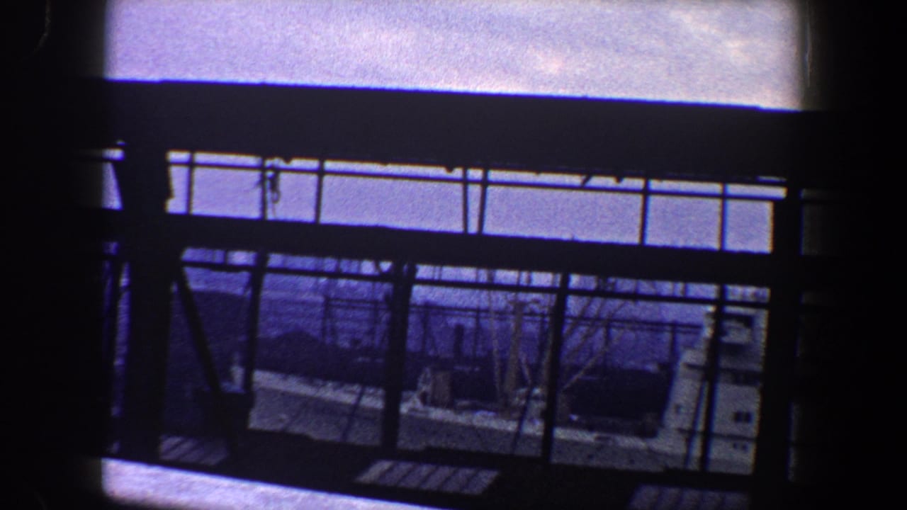 1960 New York City home-movie view through a dark ship railing toward water and a nearby vessel under bright sky.