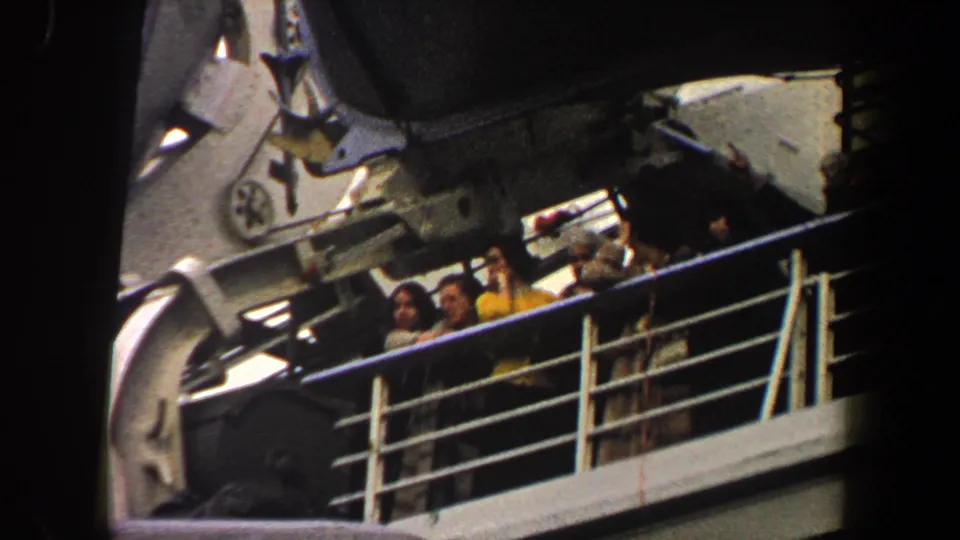 Passengers, including a woman in a yellow top, stand by white ship railings beneath large deck equipment in 1960 New York City footage.