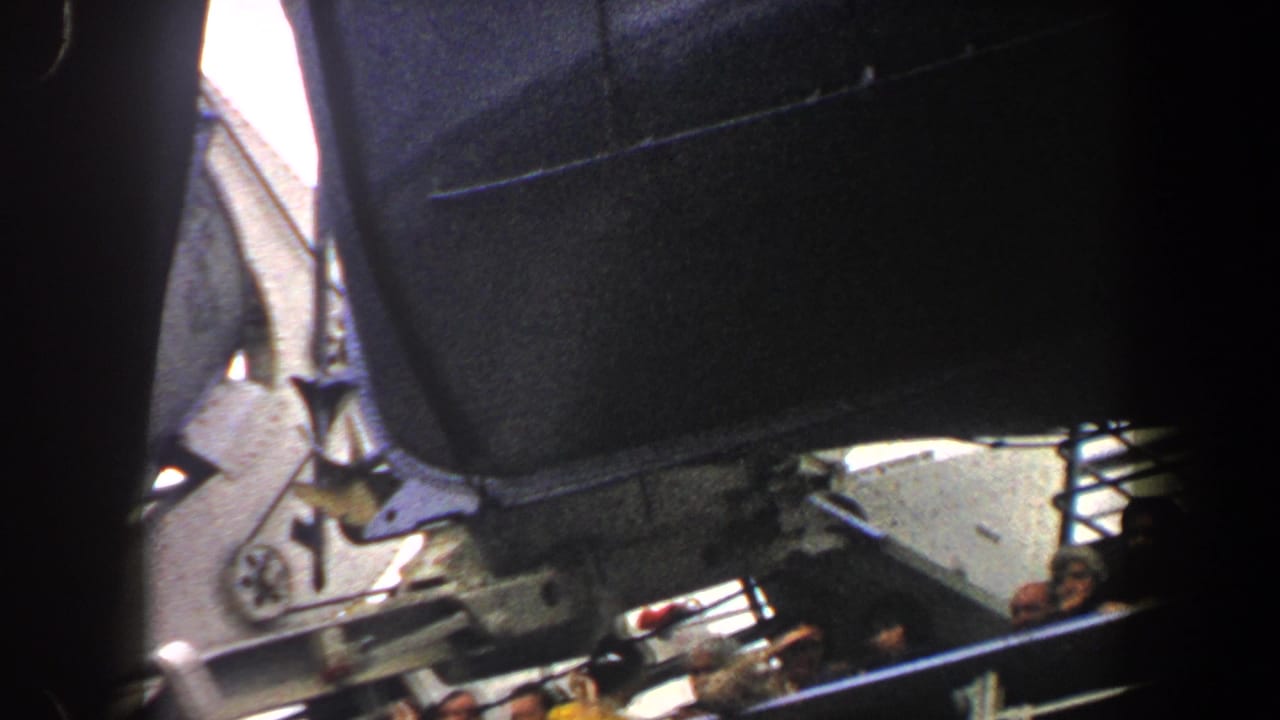 1960 New York City 8mm frame showing ship structure and railing, with passengers partly visible on a departing boat.