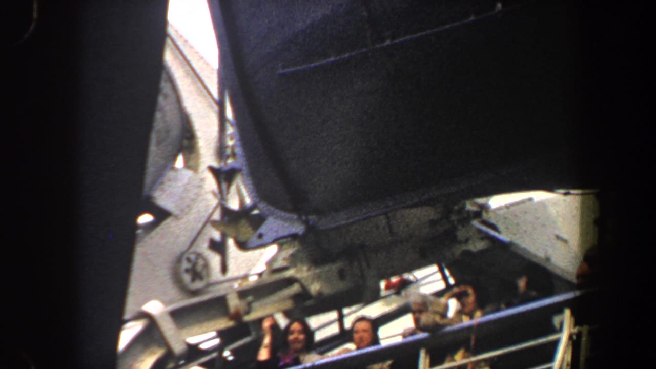 Passengers stand along a ship railing beneath dark overhead structure.