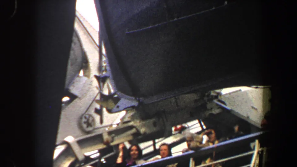 Passengers on a large boat in New York City stand near the railing, partly framed by dark ship structure.