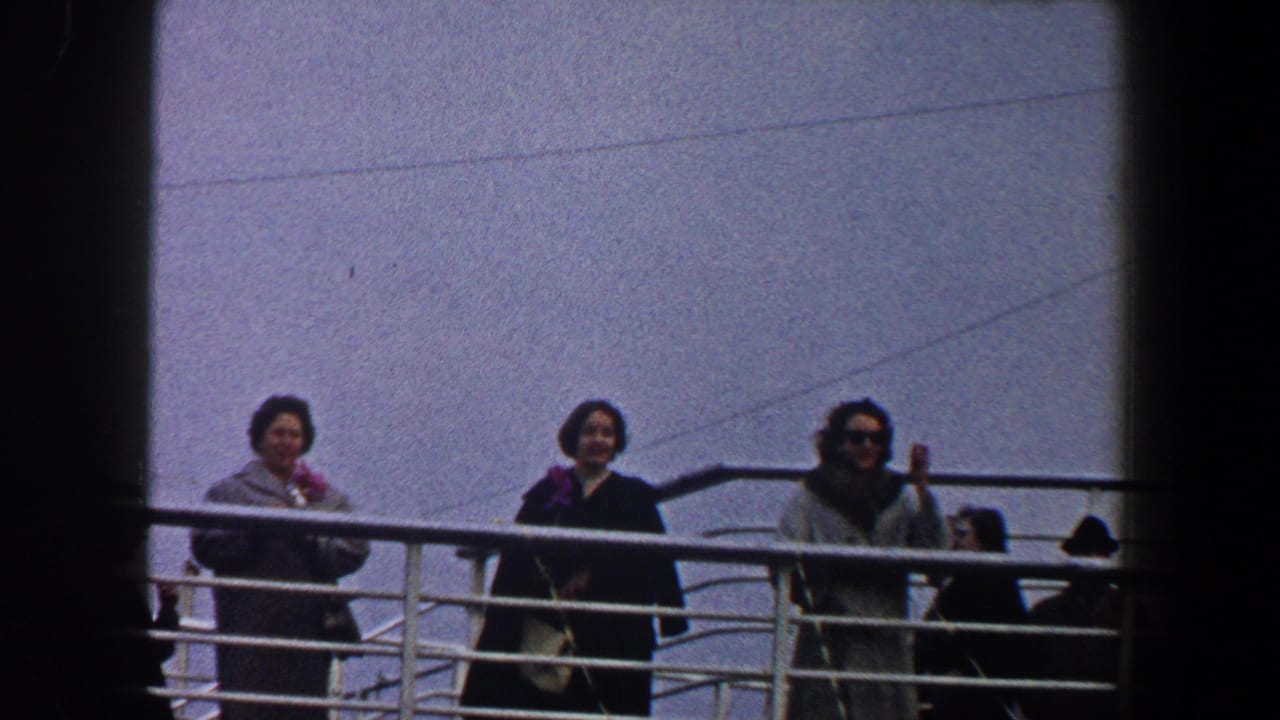 1960 New York City home-movie frame of three women in winter coats standing at a ship railing and looking toward the camera.