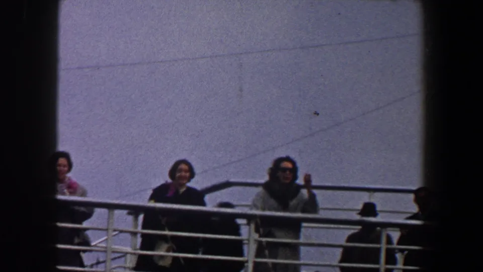1960 New York City ship-deck view with three women near a white rail, one in sunglasses, framed by dark vertical edges.