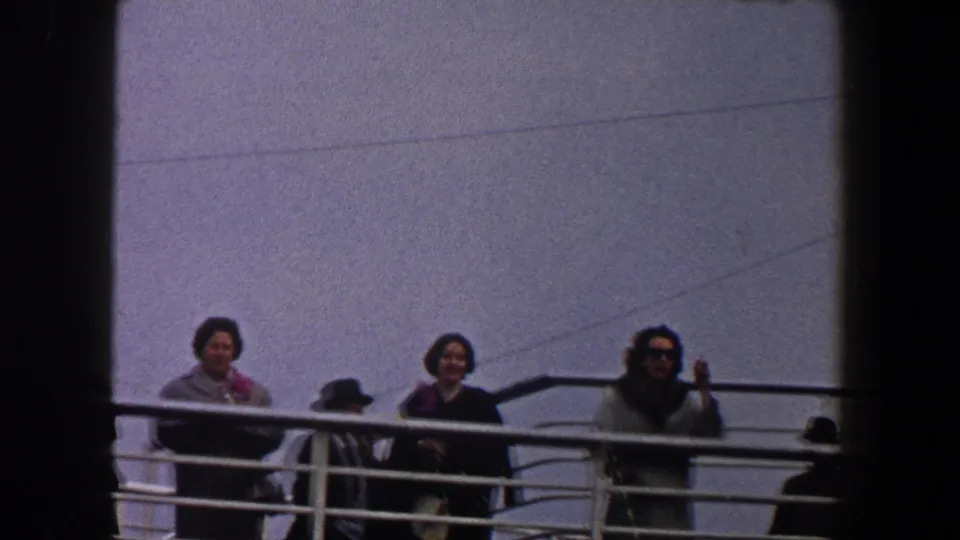 1960 New York City home-movie frame showing women at a ship rail and a hat-wearing figure moving across the deck.