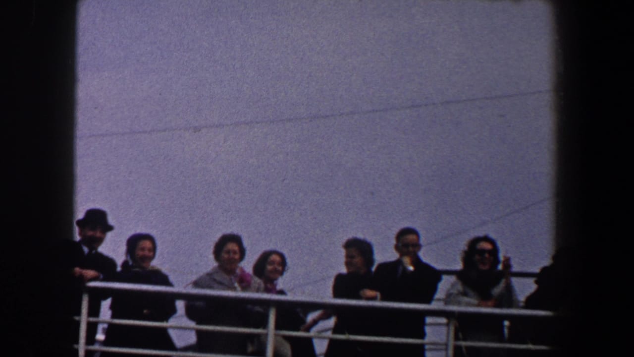 1960 New York City home-movie frame showing adults in coats, suits, and hats along a vessel railing under open sky.