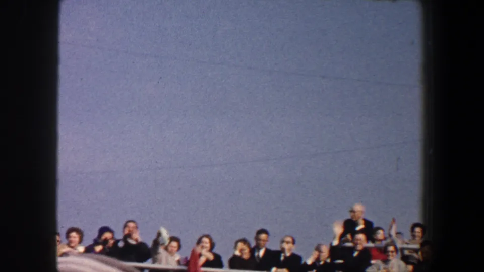 1960 New York City home-movie frame showing adults clustered along a boat railing, several waving toward the camera.