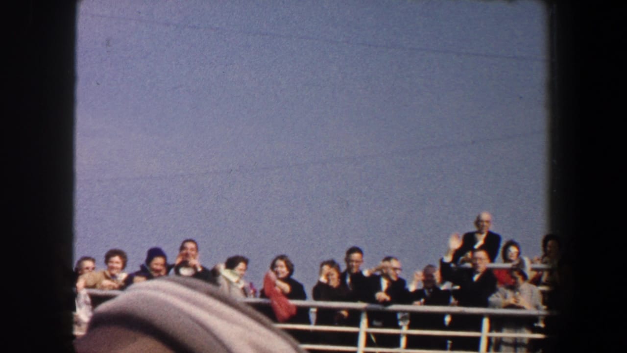 Passengers behind a boat railing wave under a blue sky, with dark 8mm frame borders visible.