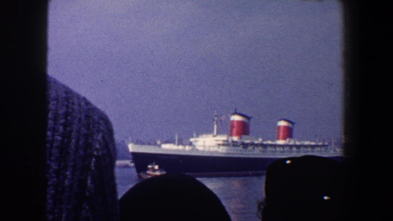 Ocean liner seen through a window with silhouetted onlookers in the foreground.