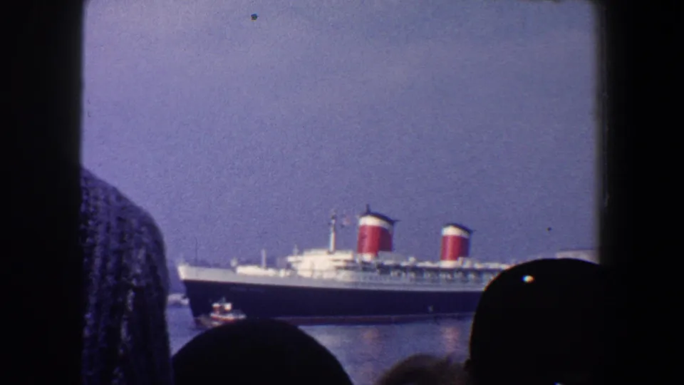 The Queen Mary appears docked in New York City harbor, with a small tugboat nearby and spectators silhouetted inside.