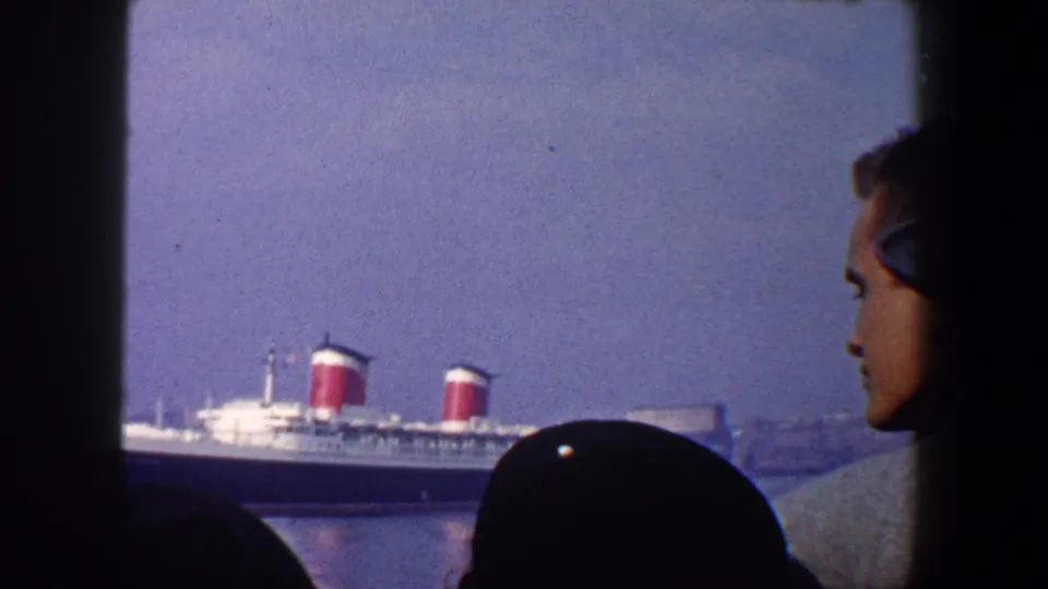 A man in profile watches the Queen Mary in New York City harbor, with window framing and other onlookers in silhouette.