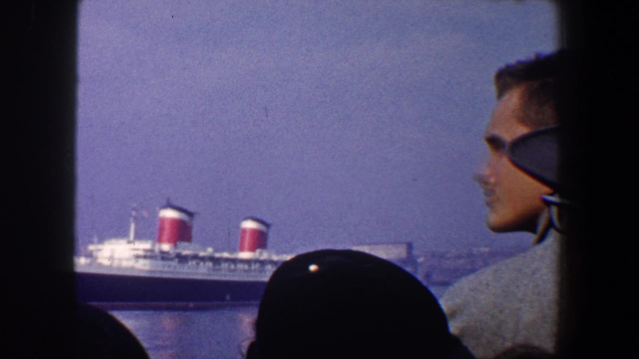 1960 New York City home-movie frame of silhouetted spectators viewing the Queen Mary across harbor water.