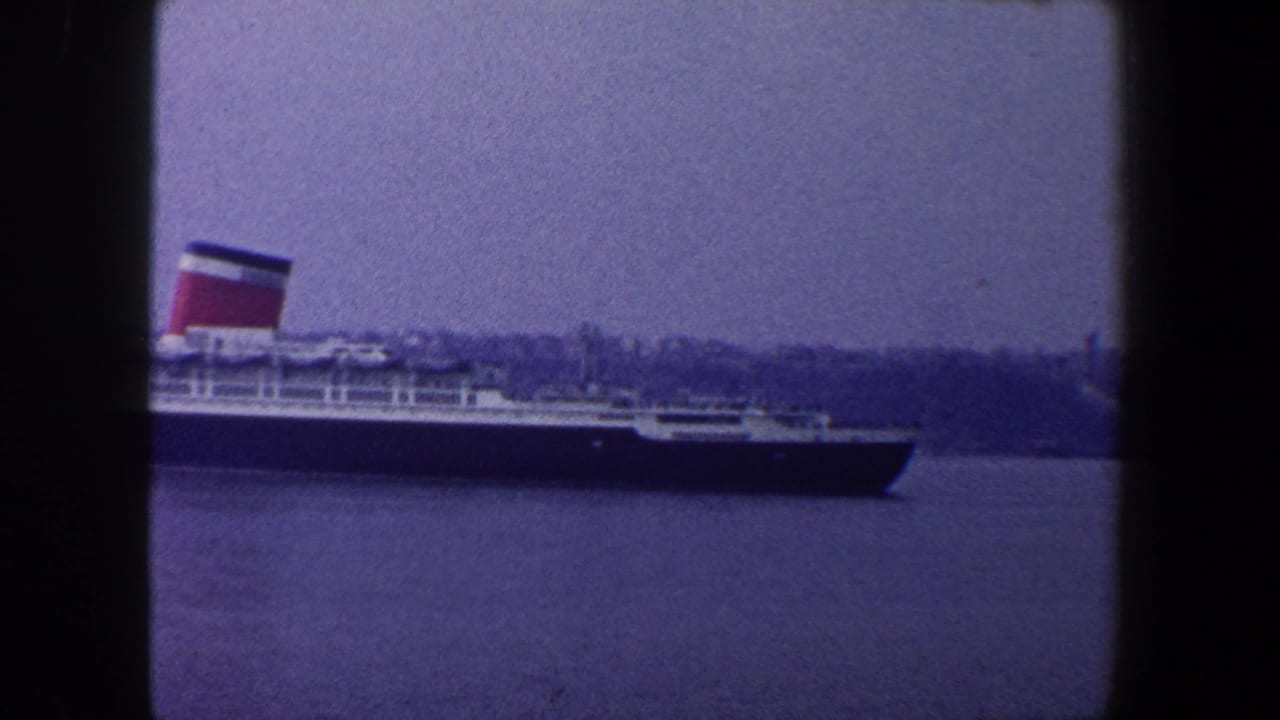 Queen Mary sits across harbor water behind a dark window mullion.