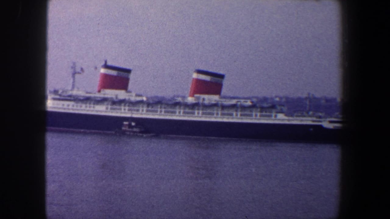 Ocean liner seen broadside with a small tugboat alongside.