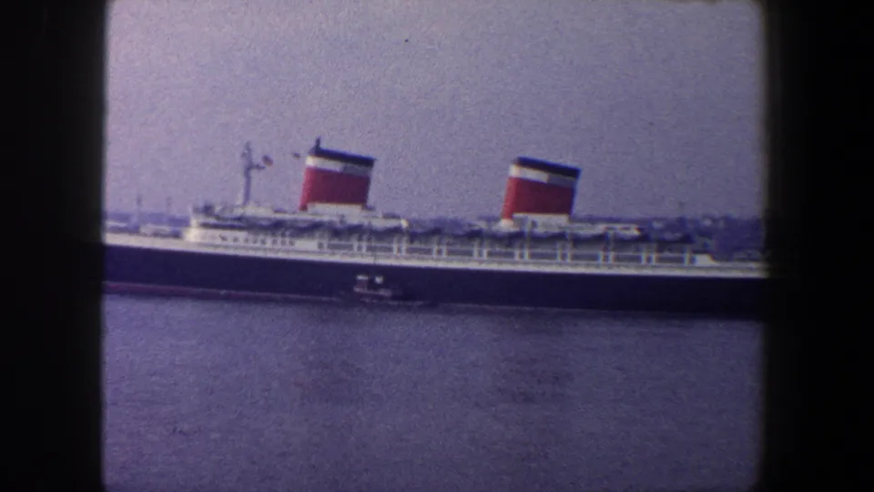 Soft 8mm frame of the liner's midsection in New York City, with two red funnels, deck railings, and a tugboat below the hull.
