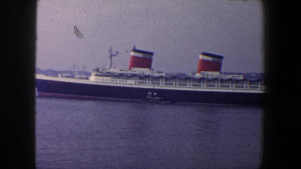 1960 New York City harbor frame showing the ocean liner broadside, red funnels above the decks, and open water below.