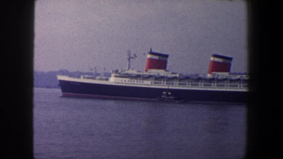 Large passenger liner in New York harbor, with two red-and-white funnels and a small tugboat near the hull.