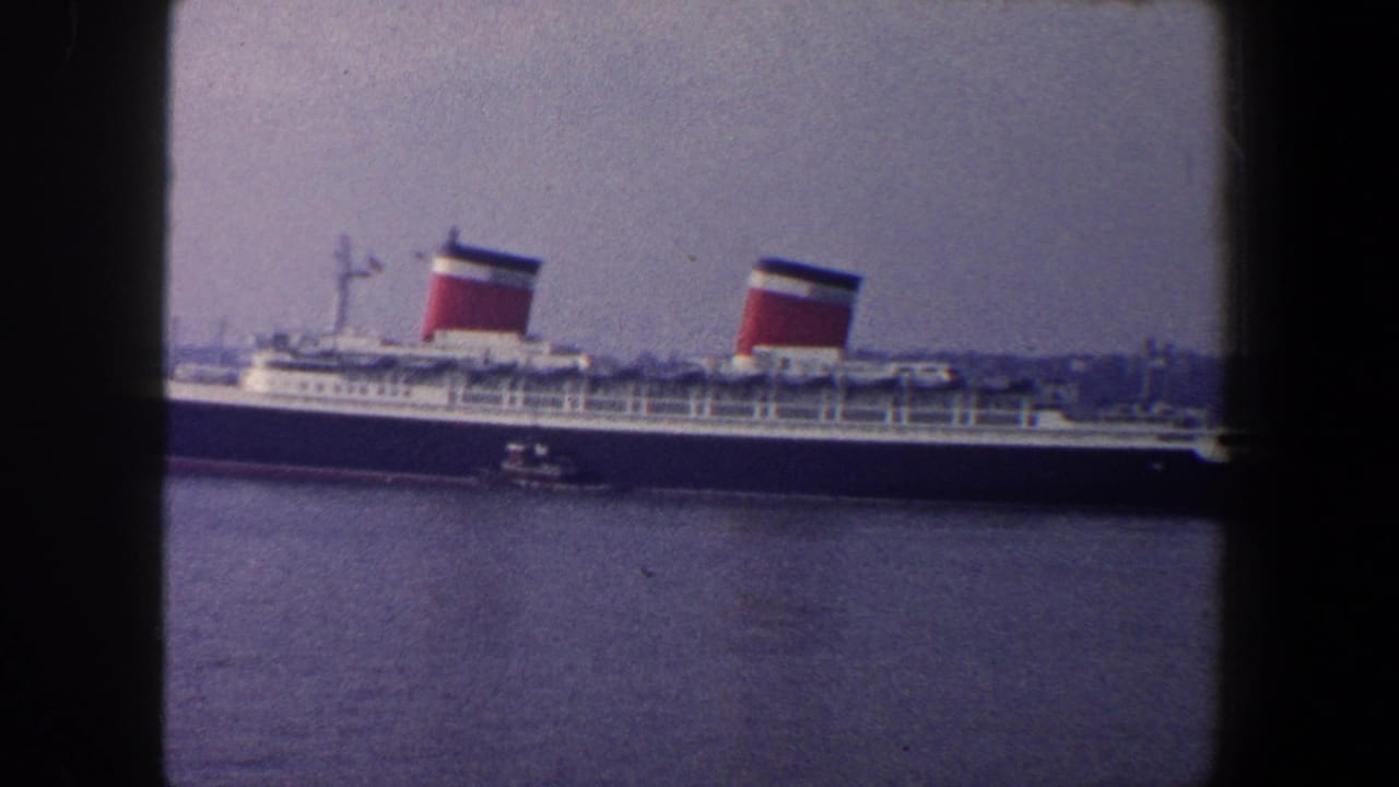 Large ocean liner with two red-topped funnels moving across harbor water.