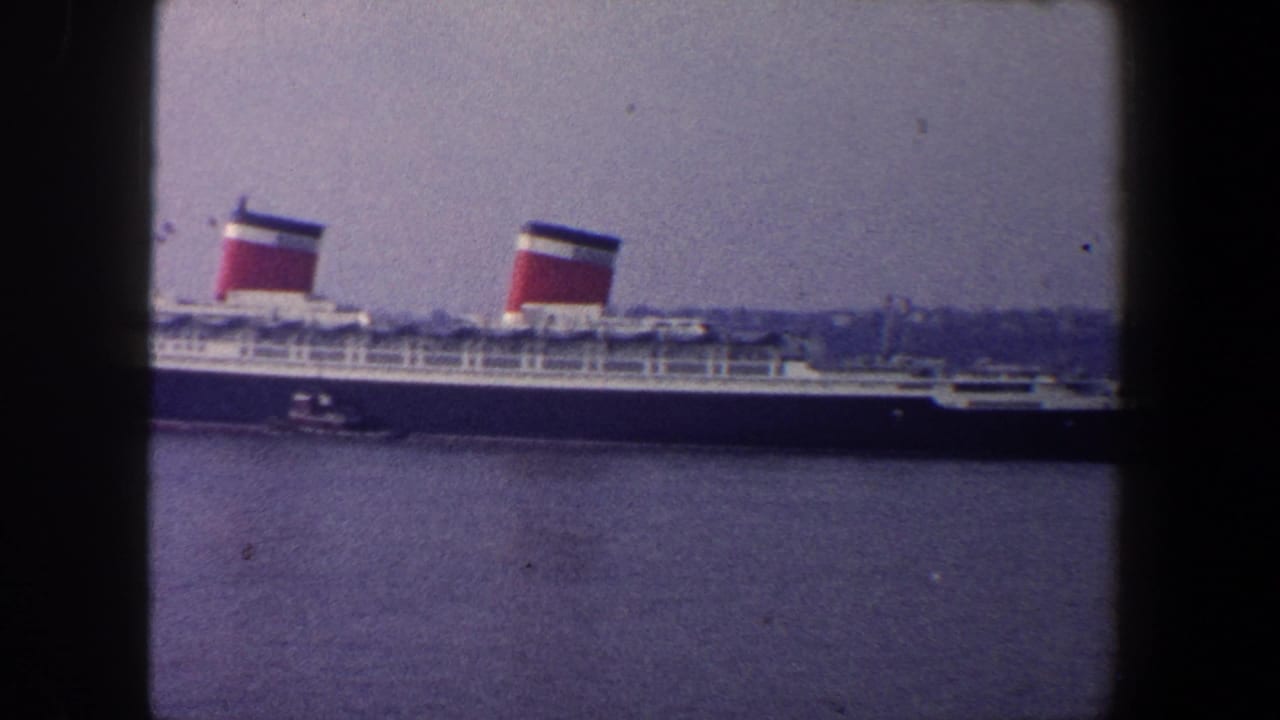Ocean liner broadside on harbor water with distant shoreline behind it.