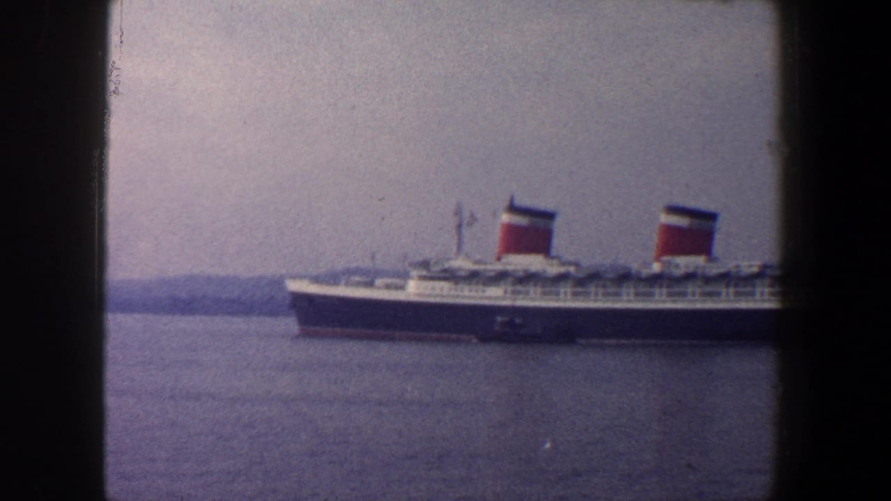 1960 New York City home-movie frame showing a large passenger liner with twin red funnels on calm harbor water.