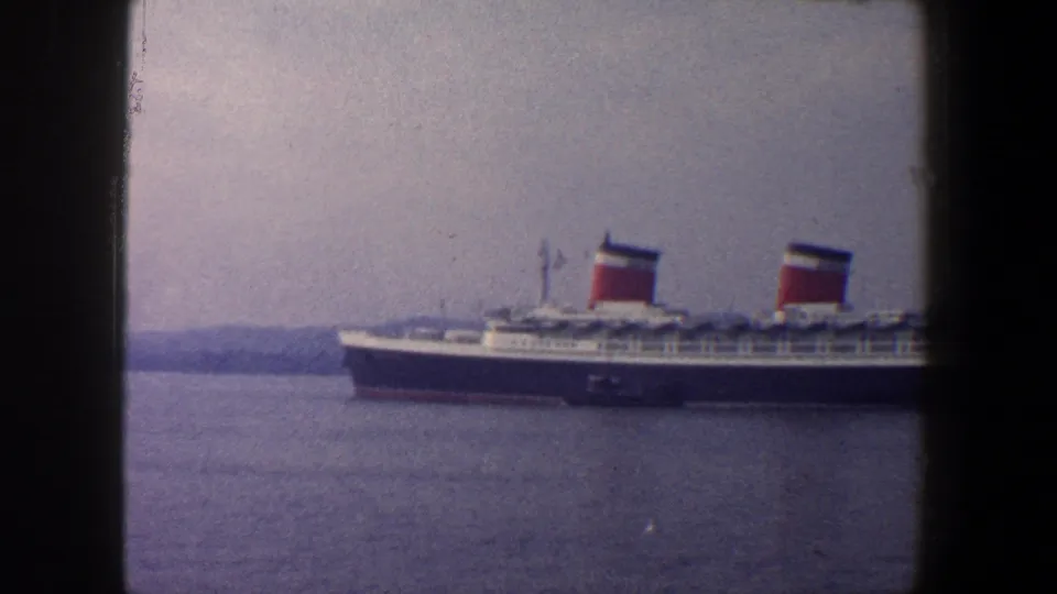 1960 New York City home-movie frame showing a large passenger liner with twin red funnels on calm harbor water.