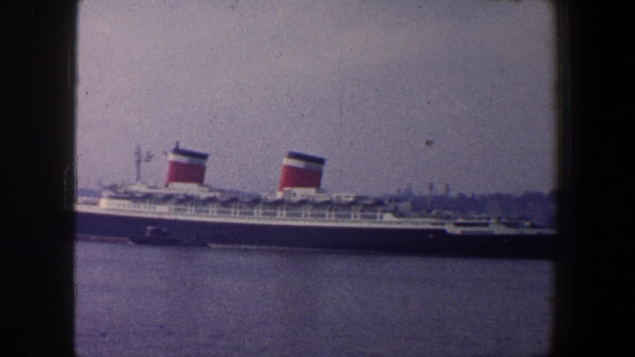 Large ocean liner with two red funnels moving across harbor water near a distant shoreline.