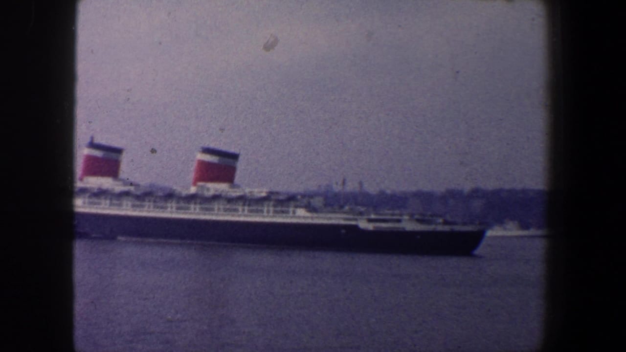 Ocean liner continues across the frame with twin red funnels and shoreline in the background.