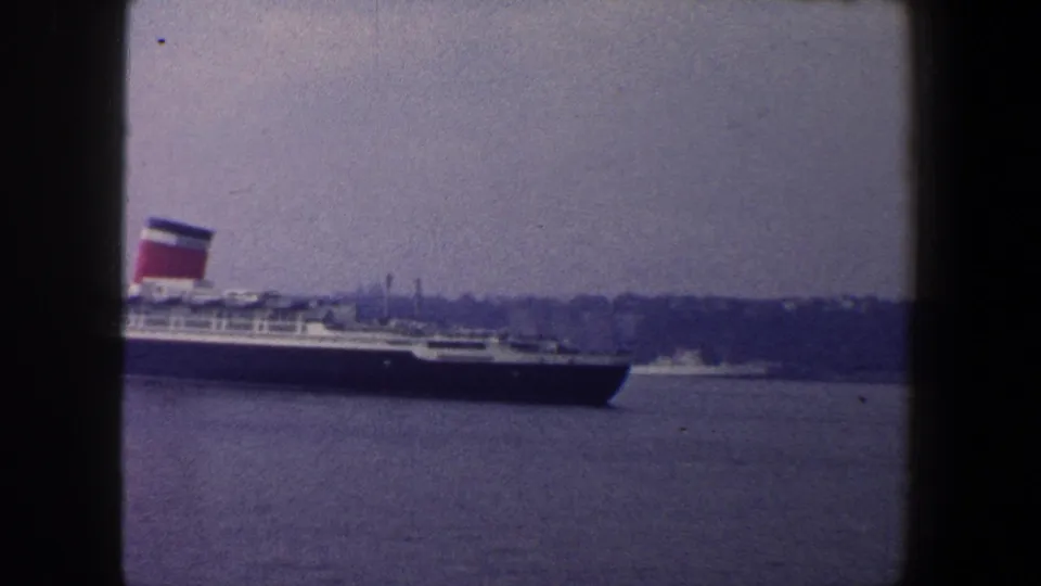 The liner is partly cropped as it moves through the harbor, with funnels, decks, water, and shoreline still visible.