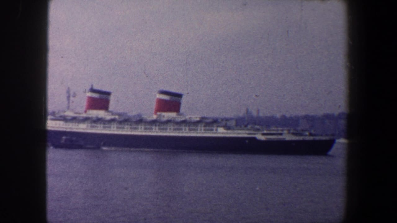 Large ocean liner on blue harbor water with two red, black, and white funnels.