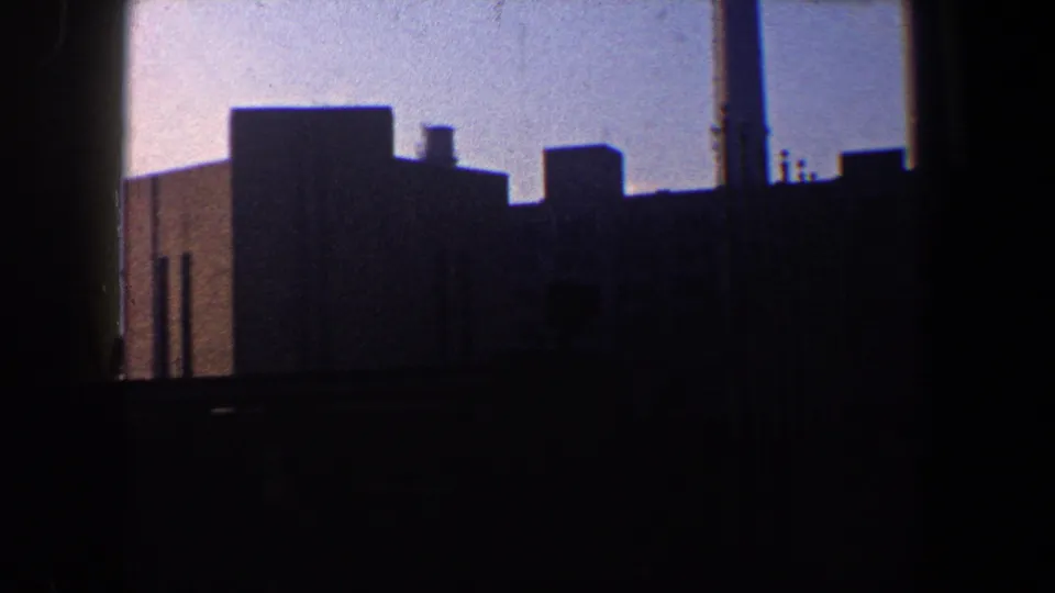 Silhouetted industrial waterfront structures in New York City, filmed from a moving 8mm home-movie viewpoint.
