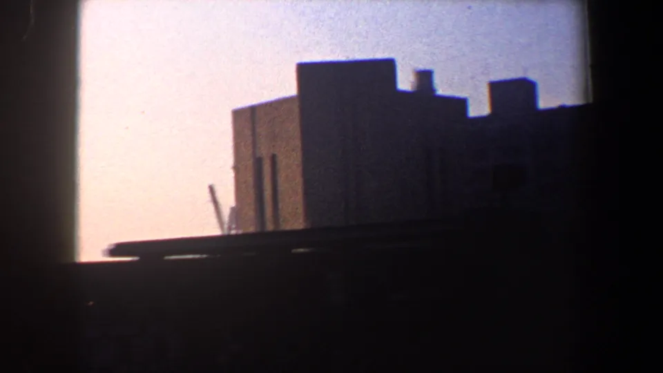 1960 New York City waterfront cutaway with a blocky industrial building, dark railing, and a crane shape near the edge.