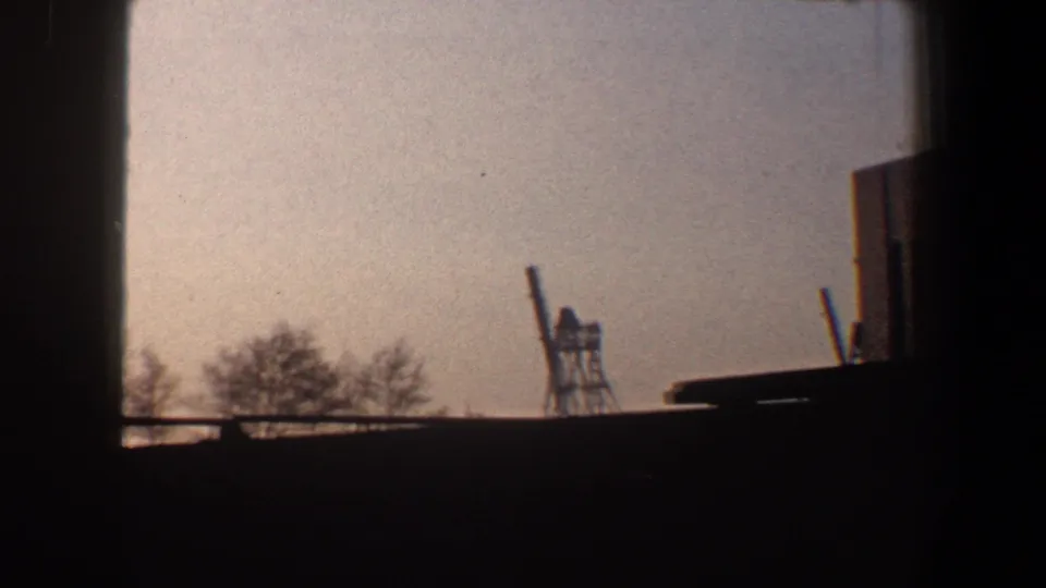 New York City waterfront silhouette with bare trees, a crane-like structure, and the edge of an industrial building.