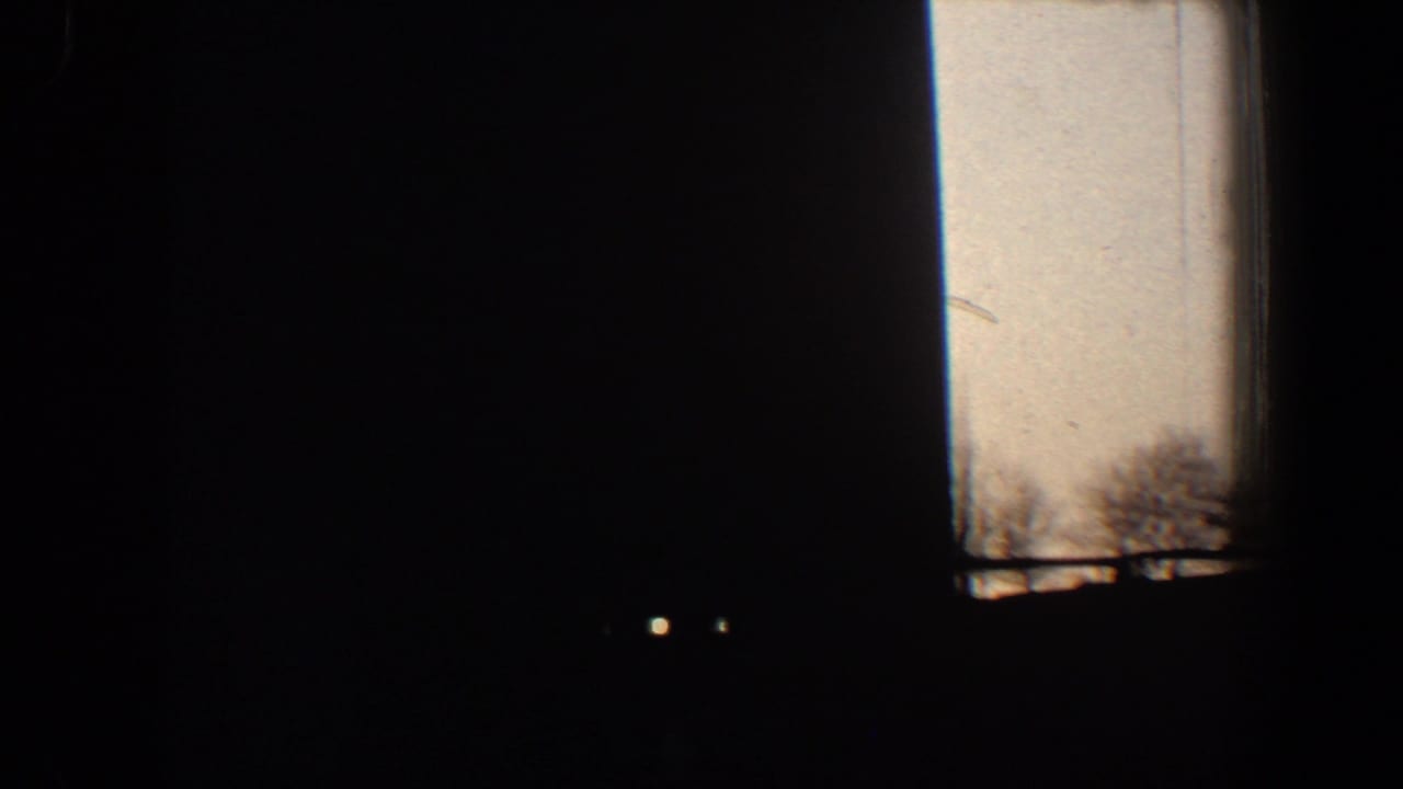 Mostly dark window view with pale sky at the side and tiny distant lights.