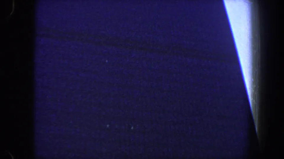 Blue-tinted 8mm frame showing a bright vertical strip near the right edge and faint urban shapes in shadow.