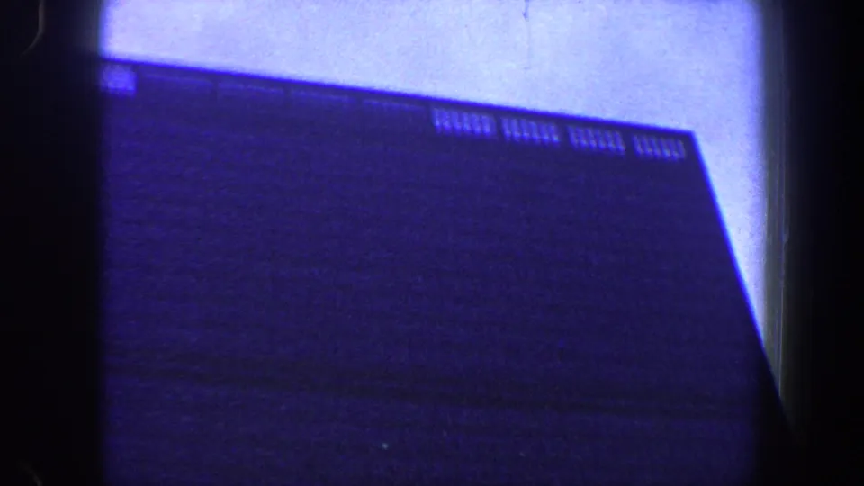 New York City 8mm frame with a dark building mass, faint window rows, and strong blue exposure from an upward angle.