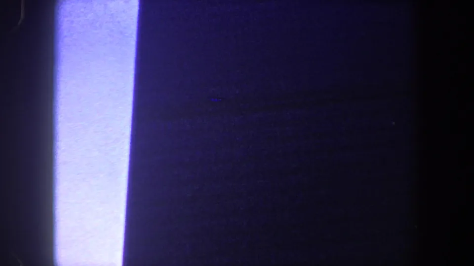 Grainy 1960 New York City 8mm frame showing dark architectural forms and a narrow bright sky strip.