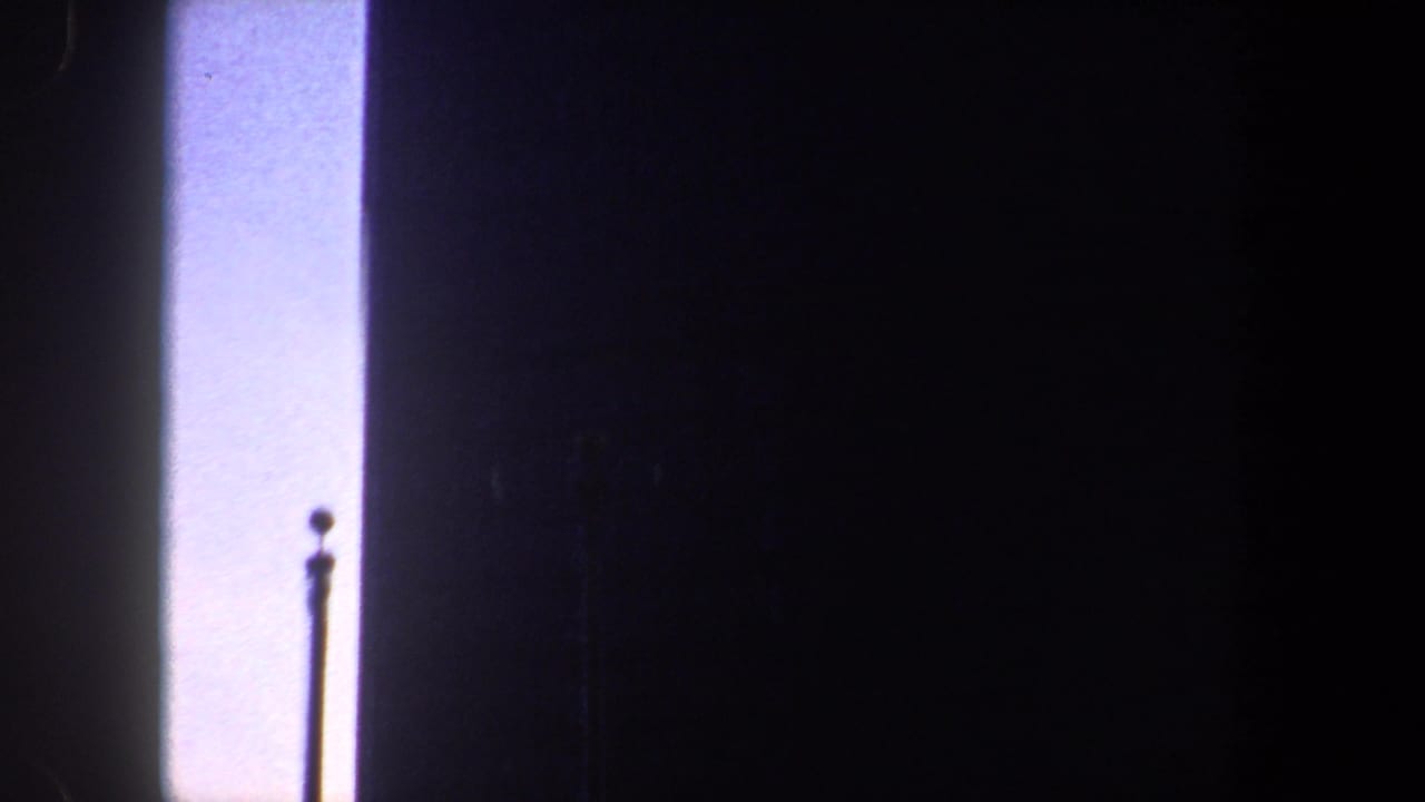 Bright vertical opening beside dark forms, with a thin pole or antenna shape near the lower edge.
