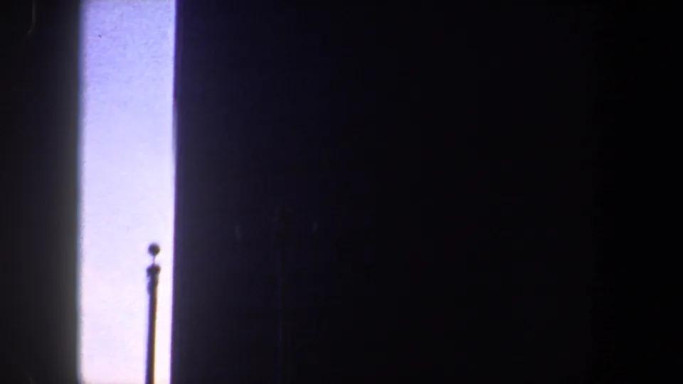 Grainy 8mm frame from the listed New York City clip with a bright vertical sky panel and a thin pole-like silhouette.