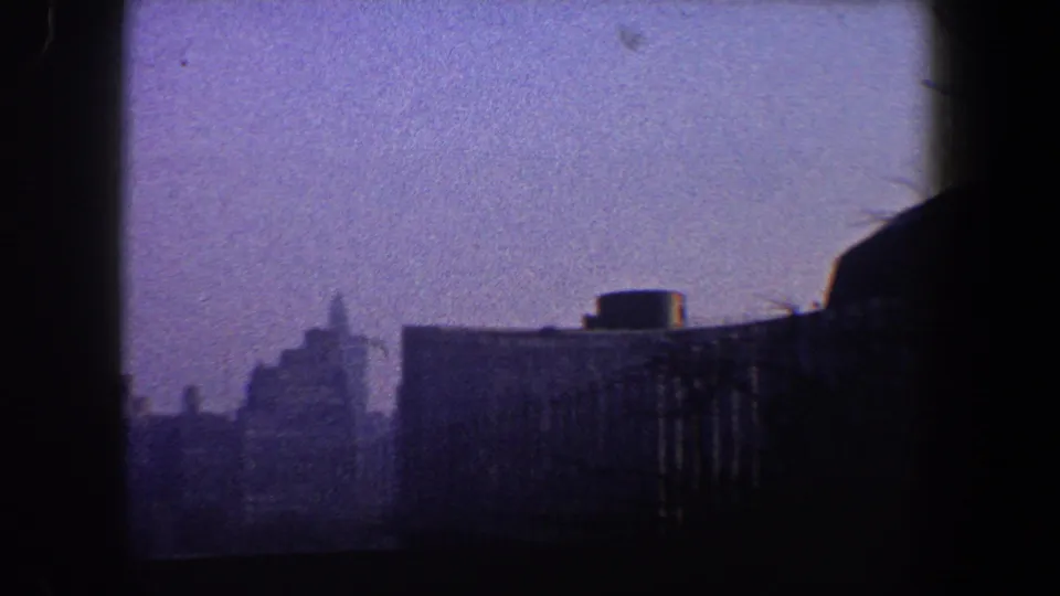 1960 New York City skyline frame with distant towers, a low rooftop structure, and a dark vertical foreground border from the shooting position.