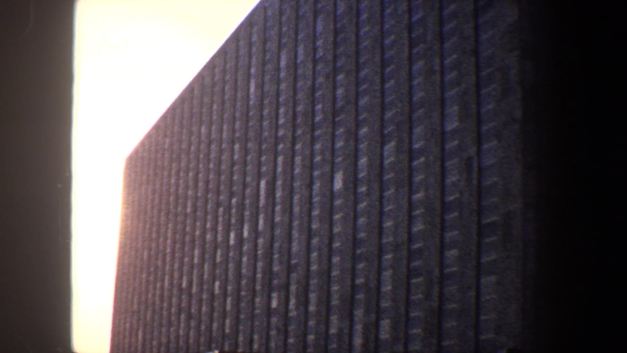Low-angle view of a dark vertically ribbed building against a bright sky.