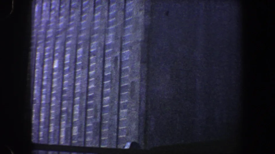 Grainy 1960 New York City 8mm frame showing a dark high-rise corner and repeated vertical facade bands.